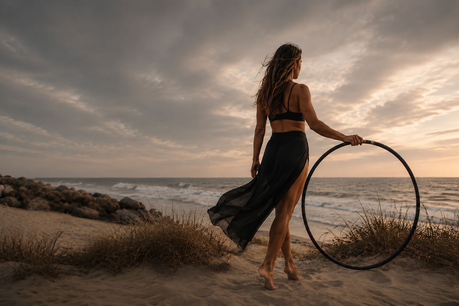 Woman with hula hoop on beach at sunset